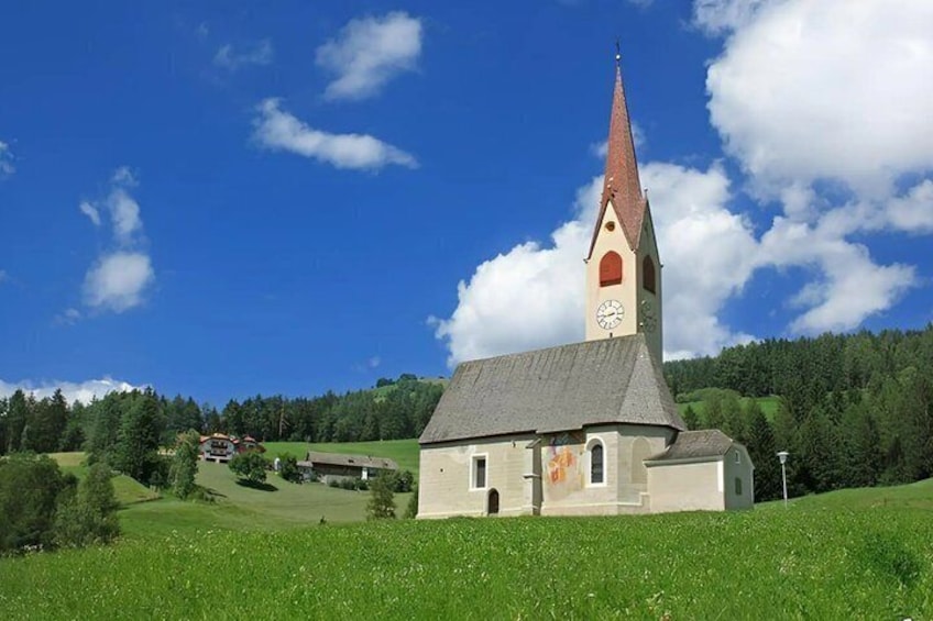 A church with a tall steeple and a clock tower, surrounded by a green landscape and a clear blue sky. 5