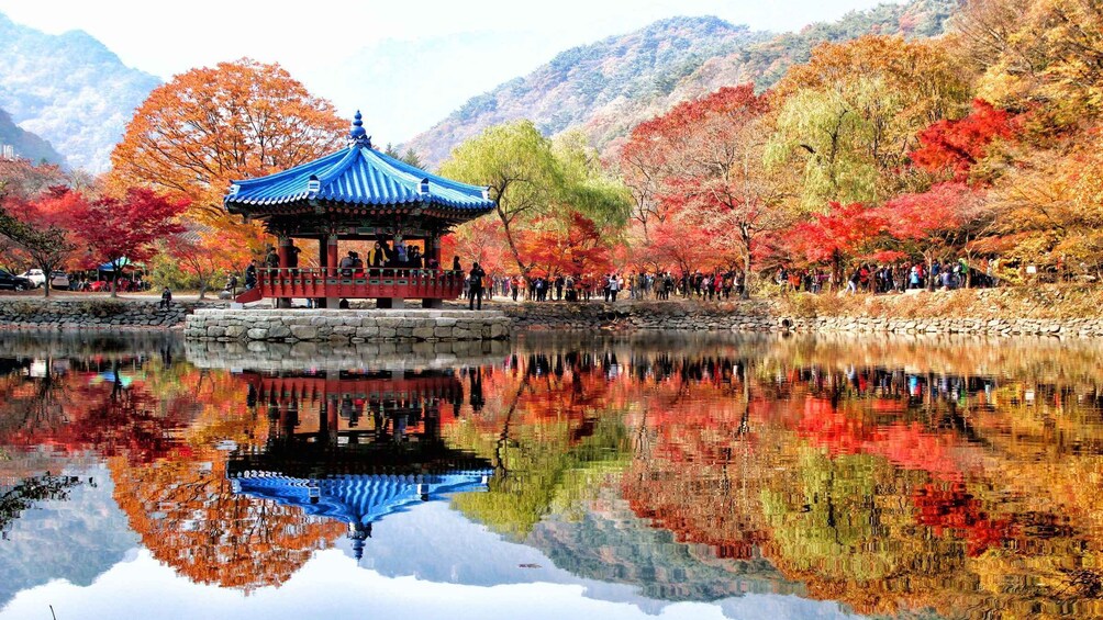 A traditional pavilion with a blue roof, surrounded by a reflective pond, and autumn-colored trees in the background. 1