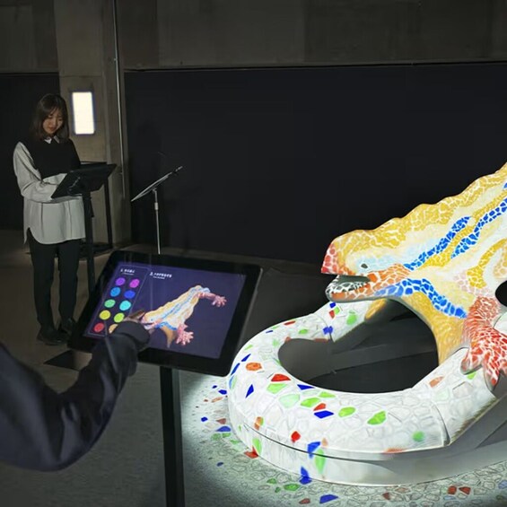 A person interacting with a touchscreen display, a colorful, abstract sculpture, and a speaker at a podium. 4
