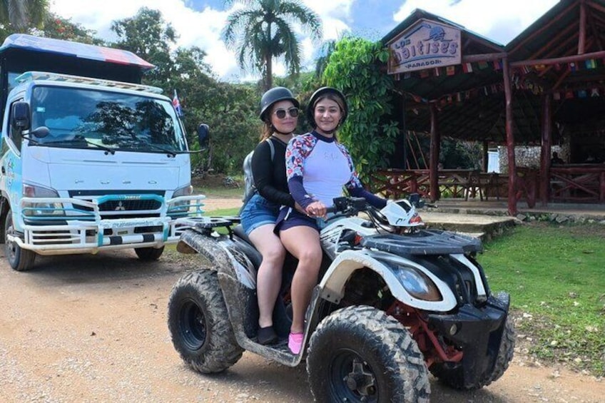 Two people on an ATV, a truck, and a building with a sign. 1