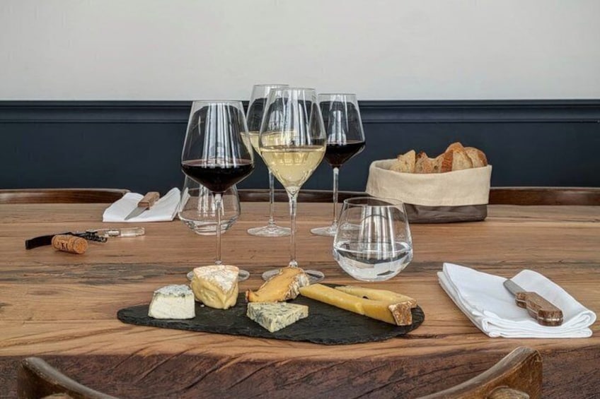 A wooden table with various cheeses, wine glasses, and a basket of bread. 1