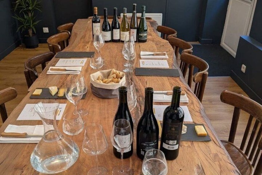 A wooden table set for a wine tasting event with bottles, glasses, and cheese. 3