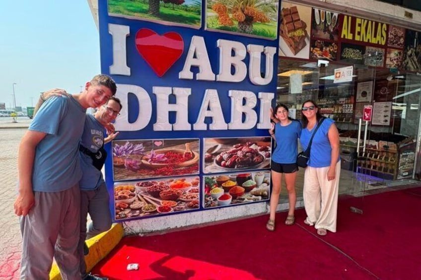 A sign with 'I ♥ ABU DHABI' and food images. 1