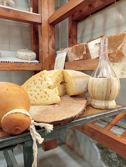 A cheese wheel, a loaf of bread, and a bottle on a wooden table. 3