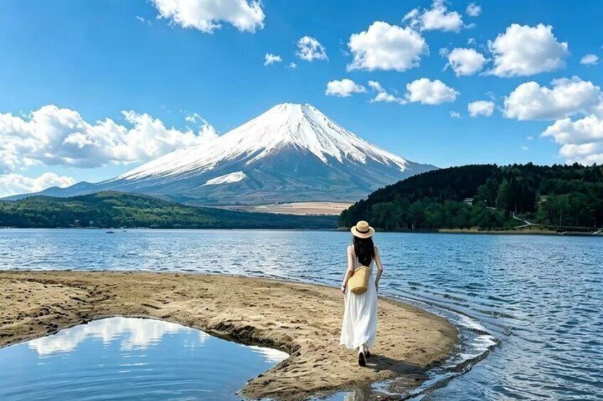 A person in a white dress and hat standing by a lake with a mountain in the background. 2
