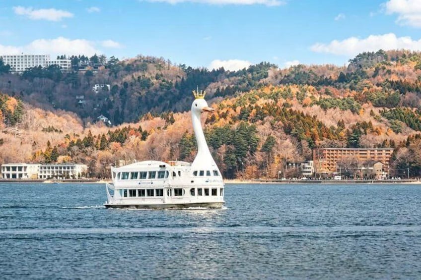 A white boat with a bird-like head on a body of water, surrounded by a forested hillside and buildings in the background. 4