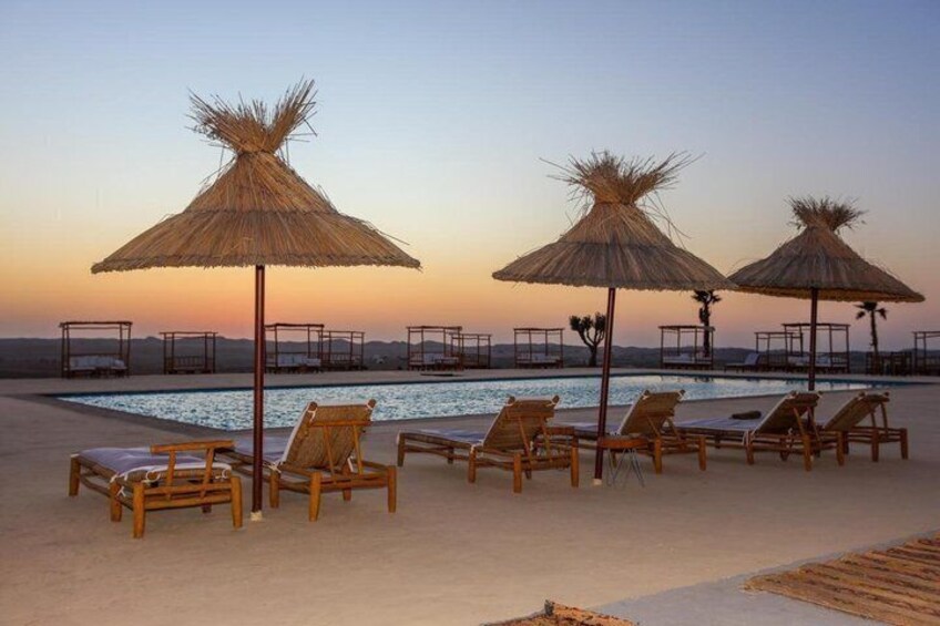 A poolside area with lounge chairs and thatched umbrellas, overlooking a body of water. 2