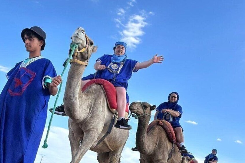 A camel with a rider, a person holding a stick, and another person sitting on a camel. 5