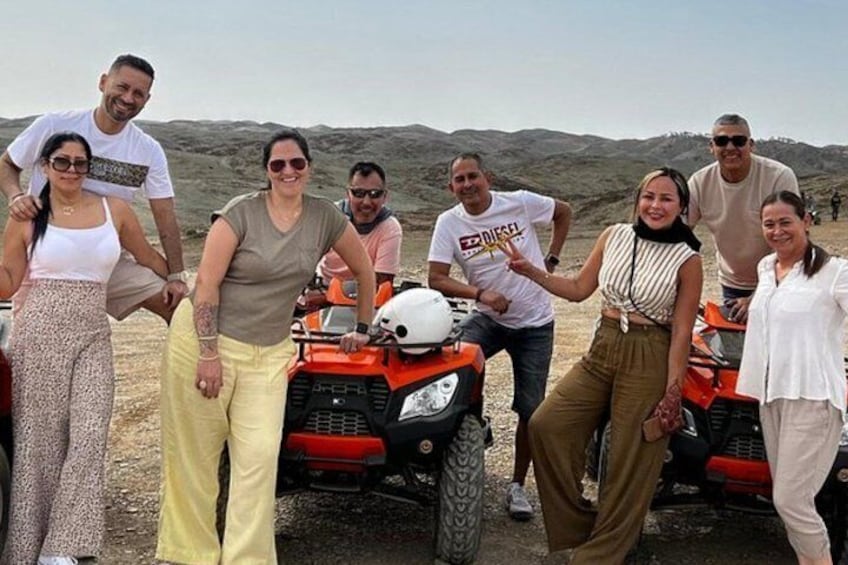 A group of people standing in a barren landscape with red off-road vehicles. 1