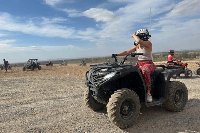 A person riding an ATV on a dirt road with other ATVs and vehicles in the background. 4