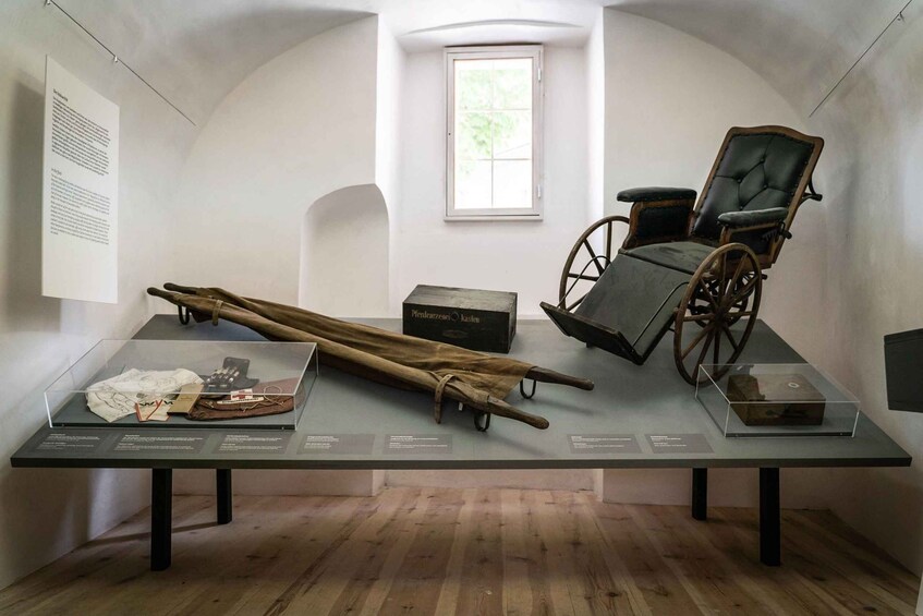 An exhibition with a wooden cart, a wheelchair, and a display case with historical items. 2