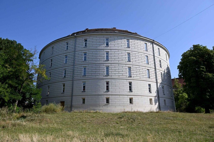 A round, multi-story building with a flat roof, surrounded by grass and trees. 1