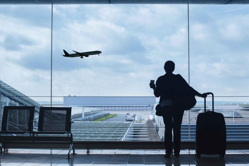 A person standing by a window at an airport, watching an airplane take off. 2
