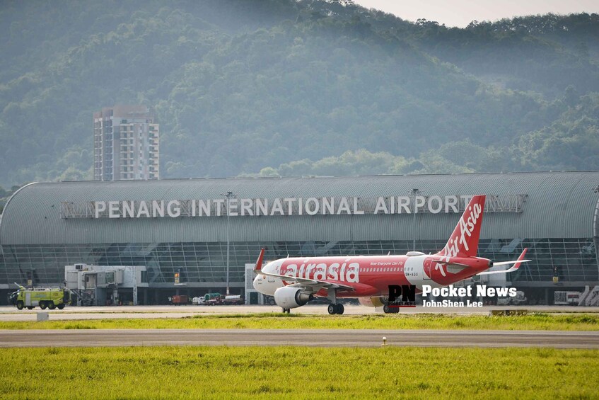 A red AirAsia airplane at Penang International Airport with a large hangar in the background. 3