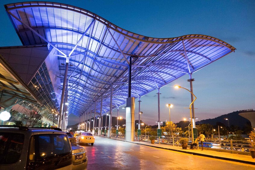 A covered pedestrian walkway with a curved roof structure, street lamps, and parked cars. 1