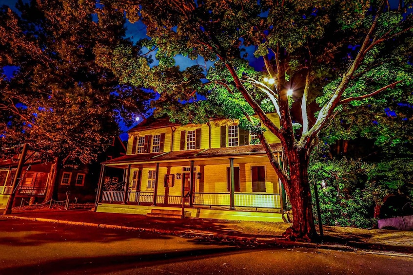 A two-story house with a porch, surrounded by trees and illuminated by streetlights. 2