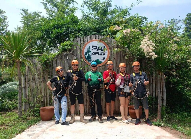 A group of people in helmets and harnesses standing in front of a sign with a logo and text. 3