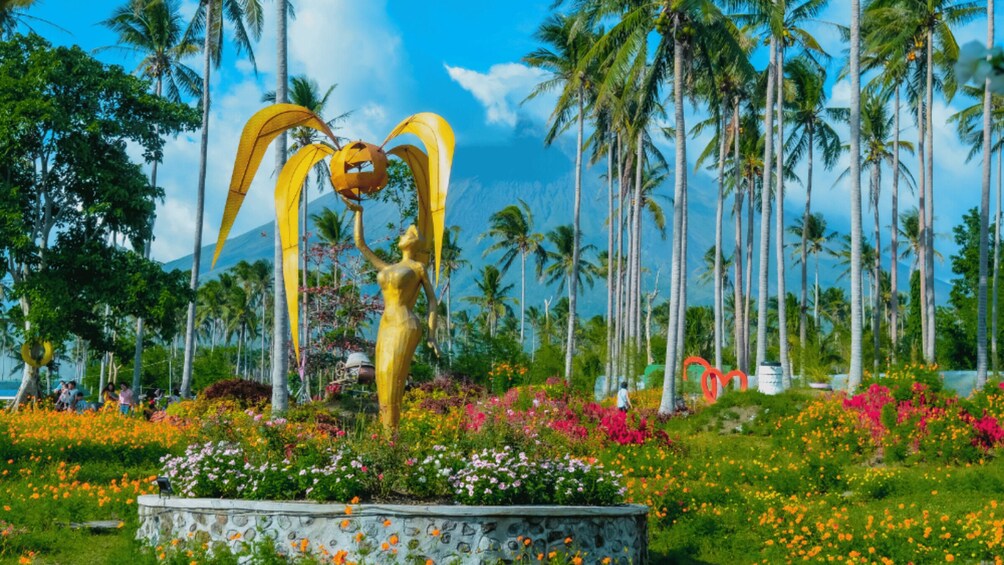A golden statue in a garden with palm trees and colorful flowers. 2