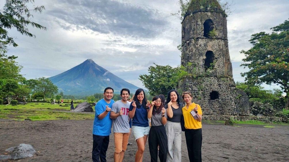 A group of people standing in front of a stone tower with a volcano in the background. 5