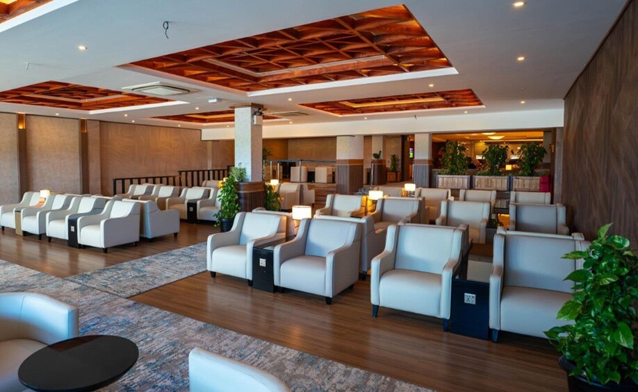 A modern lounge area with leather sofas, wooden ceiling beams, and potted plants. 3