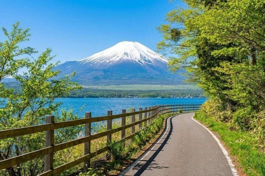 A paved road with a wooden fence, a lake, and a snow-capped mountain in the background. 3