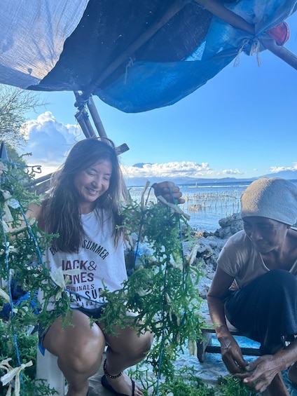 Two people outdoors, one holding a plant, with a beach and ocean in the background. 4