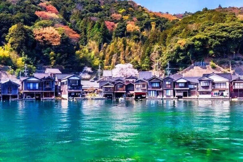 A waterfront with traditional wooden houses, clear blue water, and a forested hillside. 3