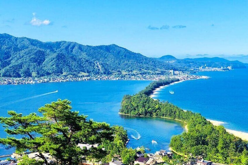 A coastal landscape with a clear blue sea, a winding road along the coast, and a forested hill in the background. 1