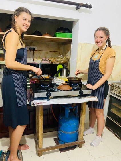 Two people cooking in a kitchen with a gas stove, pots, and a blue gas cylinder. 2