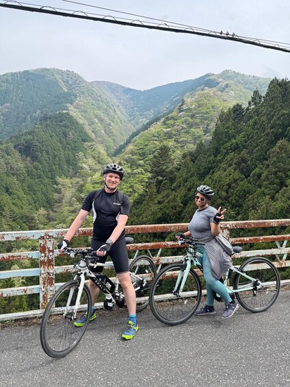 Two cyclists on a bridge with a mountainous landscape in the background. 5