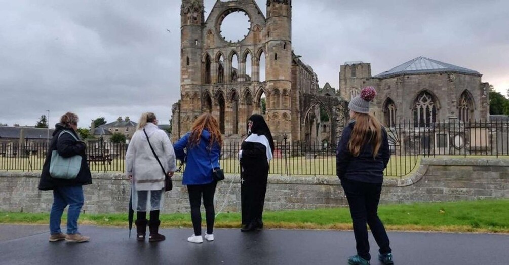 A group of people standing in front of a historic stone structure with a large circular window and arched windows. 3