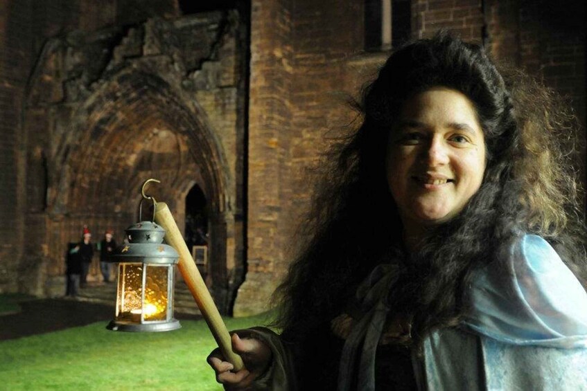 A person holding a lantern in front of an old stone building with an arched doorway. 2
