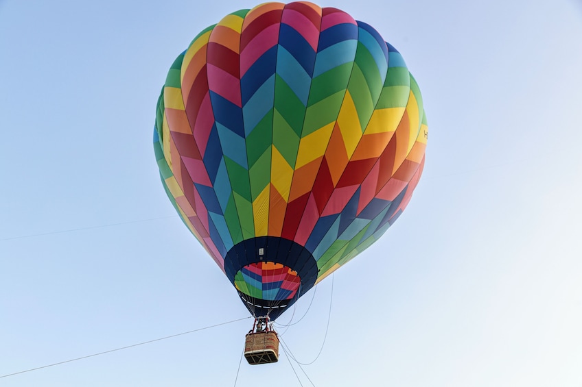 A hot air balloon with a multicolored pattern, ascending into a clear sky. 1