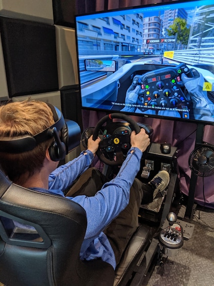 A person in a racing simulator setup with a steering wheel, pedals, and a monitor displaying a racing game. 2