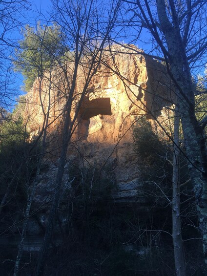 A rocky cliff with a large wooden cross, surrounded by trees and under a clear sky. 4