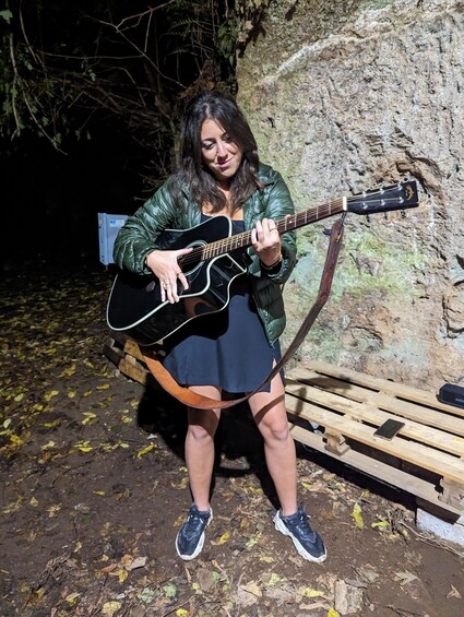 A person playing a black guitar outdoors. 3