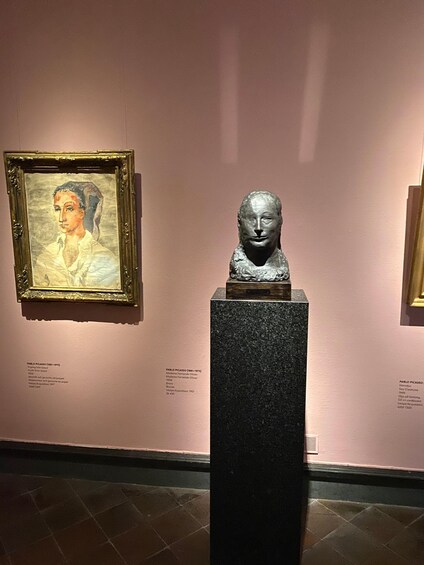 A museum exhibit with a framed painting and a bust sculpture. 5