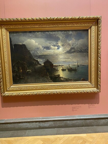 A framed painting of a coastal scene with boats, a lighthouse, and buildings. 3