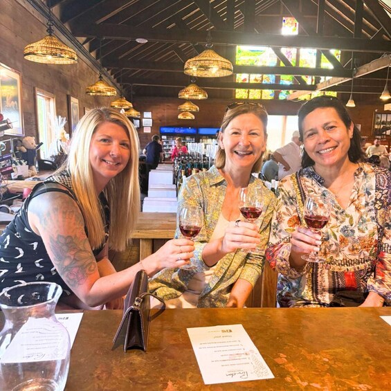 Three people sitting at a table with wine glasses, in a restaurant with hanging lights and stained glass windows. 4