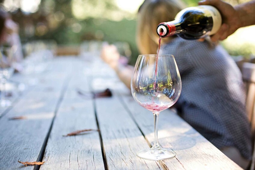 A wine bottle pouring red wine into a glass on a wooden table. 2