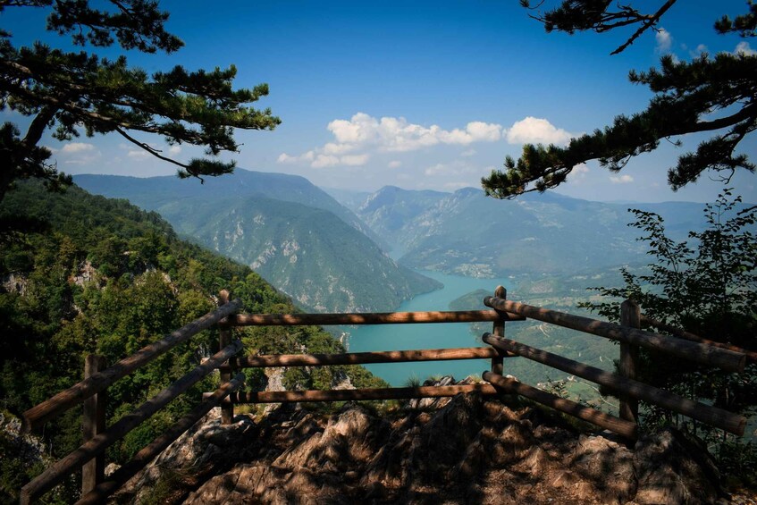 A mountainous landscape with a wooden fence, dense forest, and a lake. 4