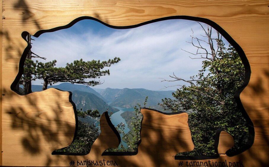 A wooden cutout of a bear with a scenic landscape view through it, including mountains and a lake. 1
