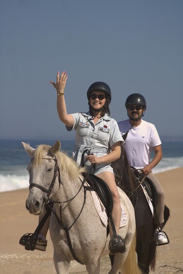 Two people riding horses on a beach with the ocean in the background. 3