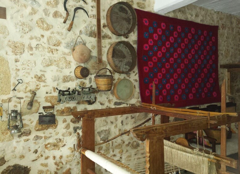A rustic room with a stone wall, a wooden loom, and various traditional tools and textiles. 5