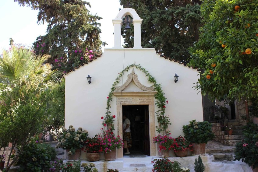 A small white church with a bell tower, surrounded by lush greenery and flowering plants. 3