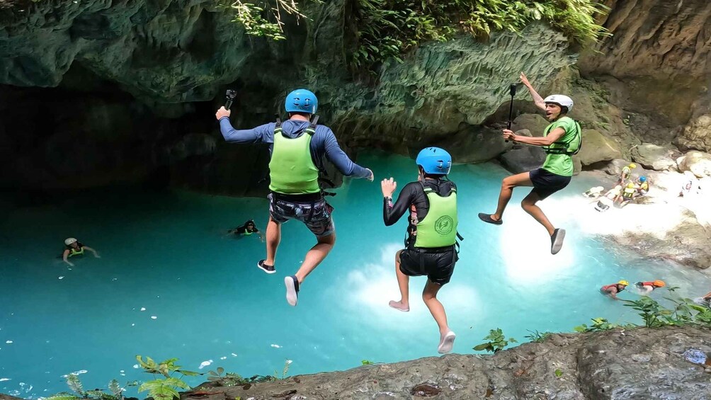 People jumping into a clear blue pool from a rocky cliff. 1