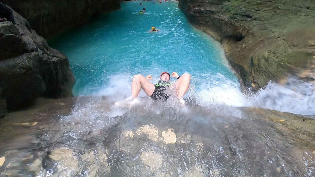 A person sliding down a water slide into a pool surrounded by rocky terrain. 3