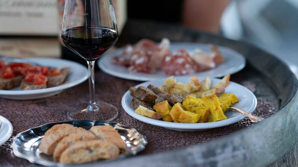 A table with plates of food, a glass of red wine, and a bottle in the background. 2