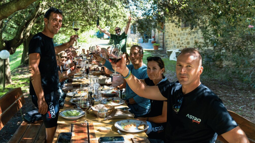 A group of people sitting at an outdoor table with food and drinks, under a tree. 3
