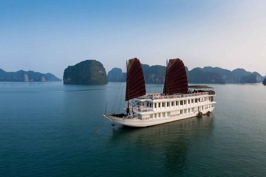 A white river cruise boat with two large sails, floating on calm water with several islands in the background. 1